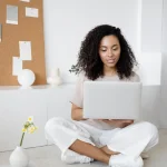 mulher negra sentada no chão de forma confortável, mexendo no computador