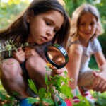 Criança com lupa explorando a natureza, representando o aprendizado em contexto naturalístico.